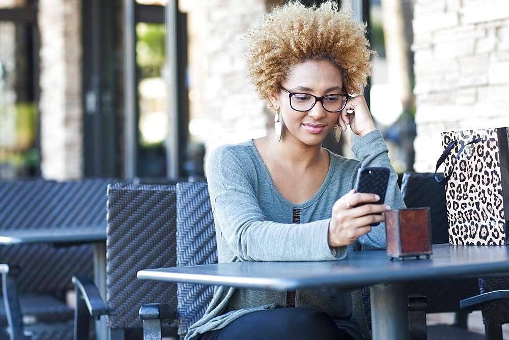 Black woman using cell phone at cafe