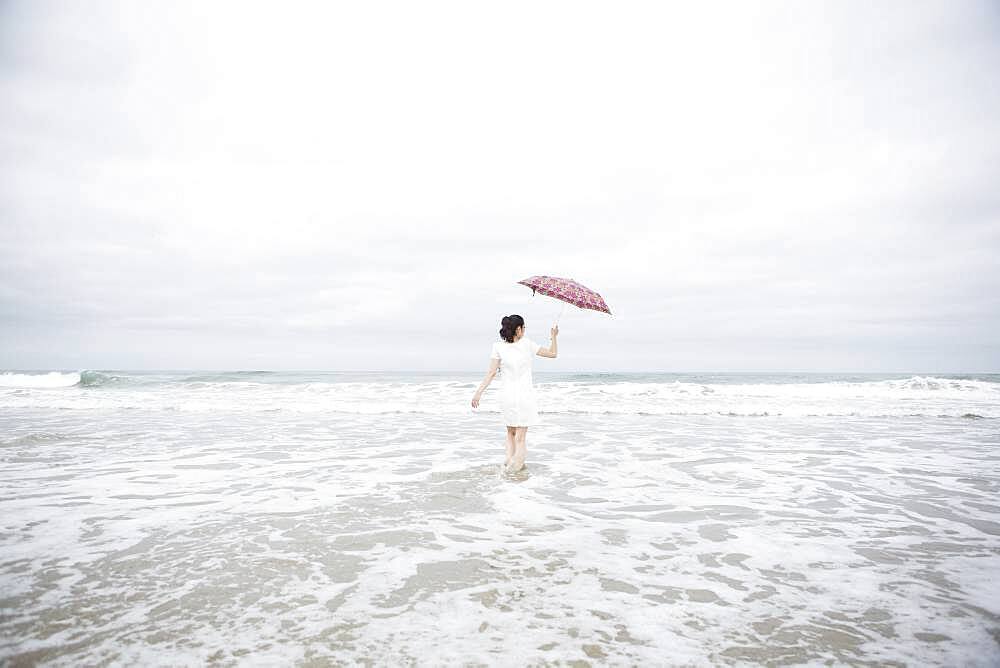 Woman wading with umbrella on beach