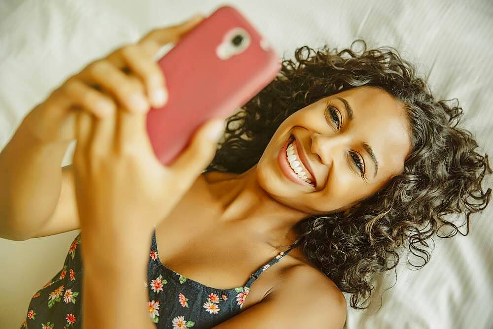 Woman taking selfie with cell phone on bed