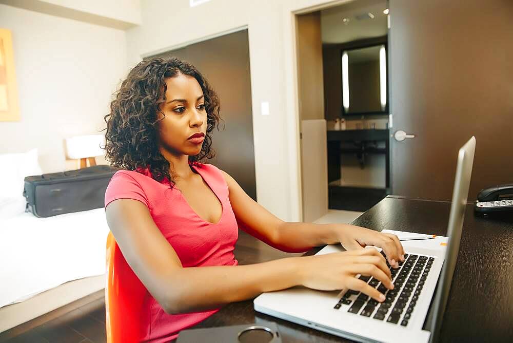 Woman using laptop at desk in hotel room