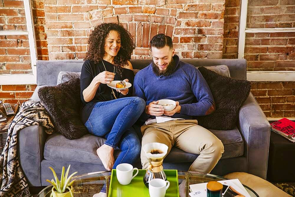 Couple eating breakfast on sofa in living room