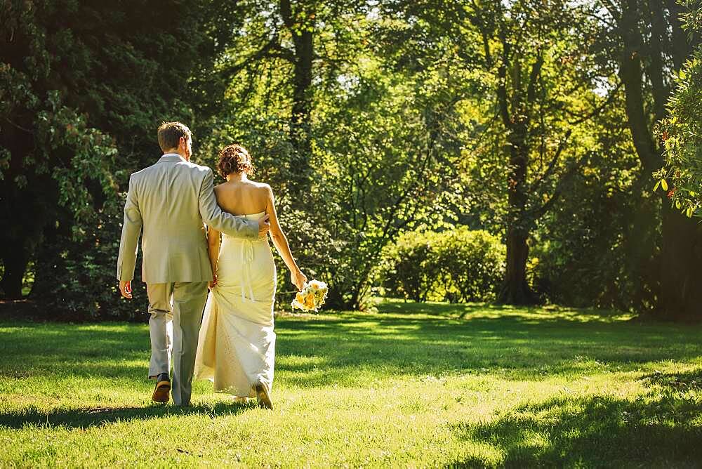 Caucasian bride and groom walking in grass