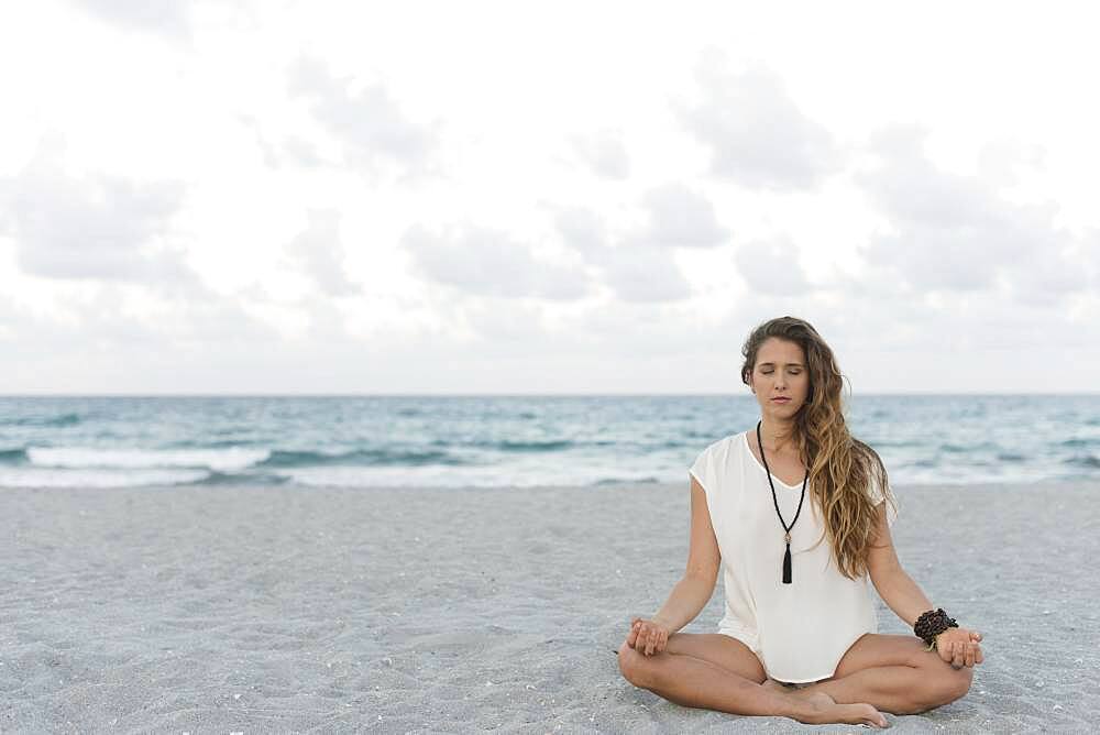 Hispanic woman meditating on beach