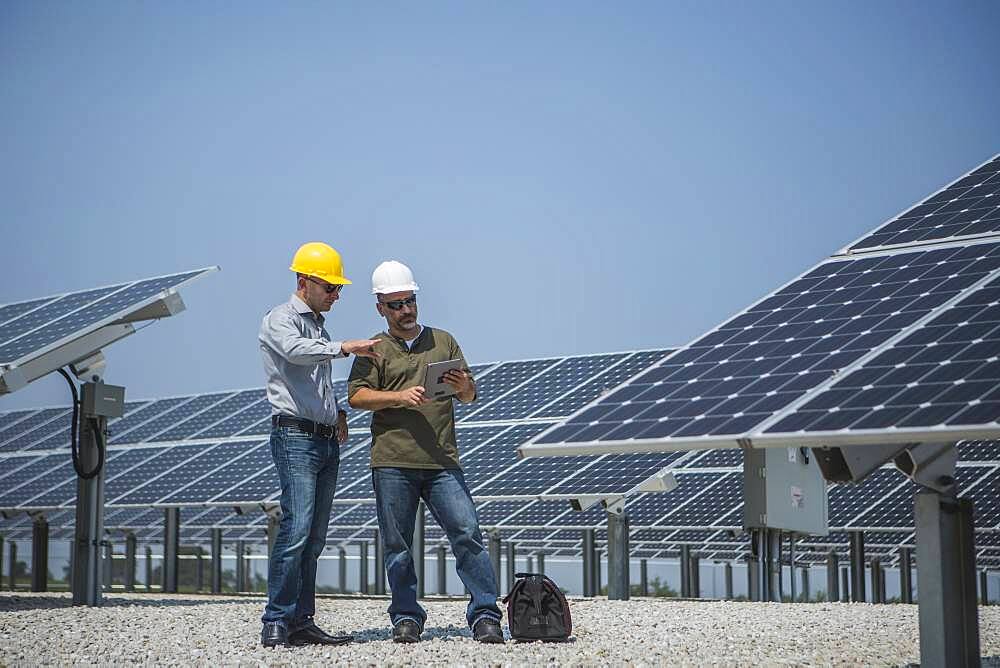 Caucasian technicians talking near solar panels