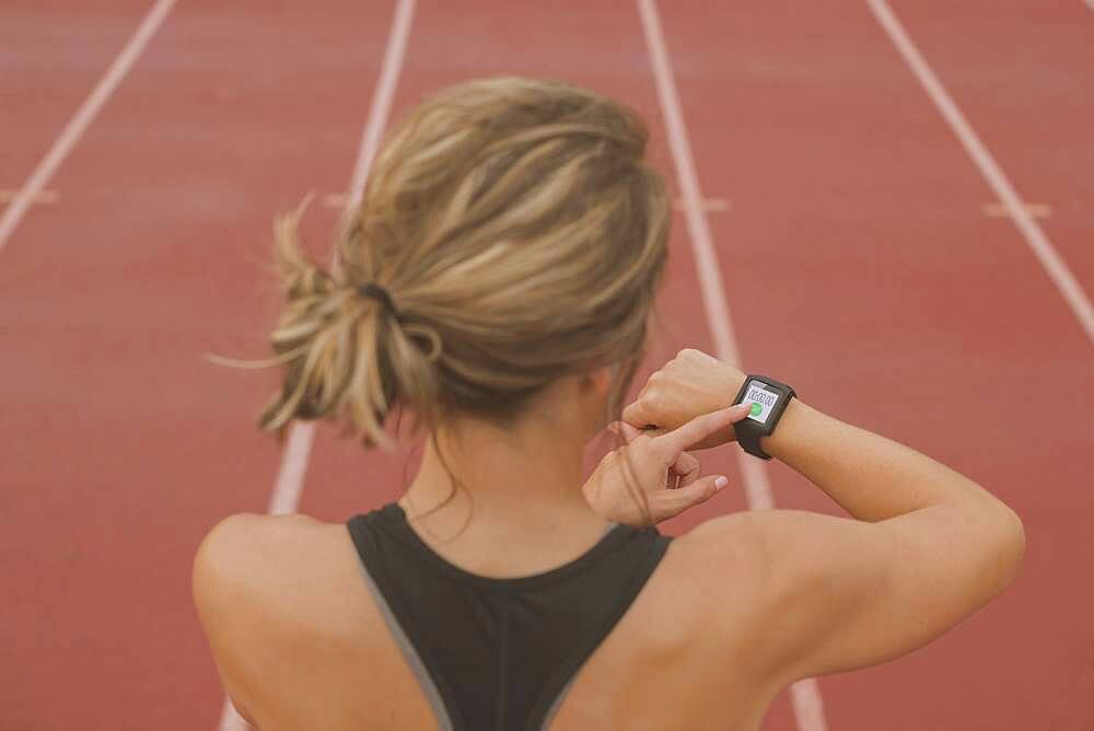 Caucasian runner checking watch on sports field