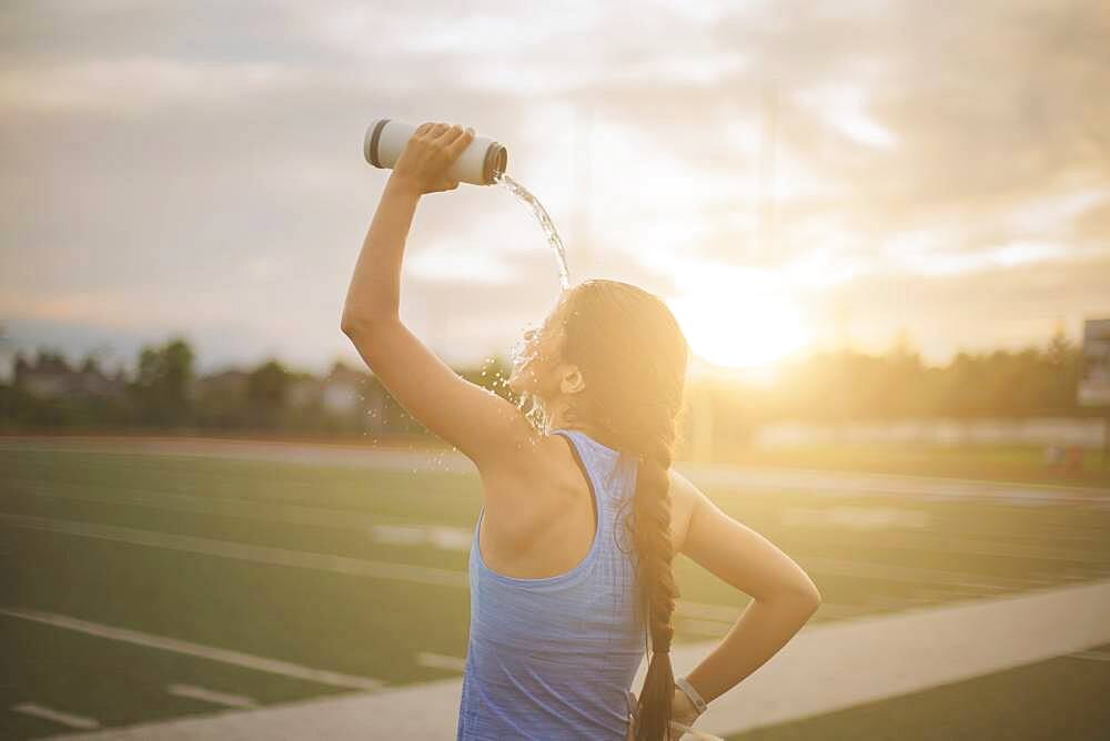 Mixed race athlete pouring water bottle on herself on sports field