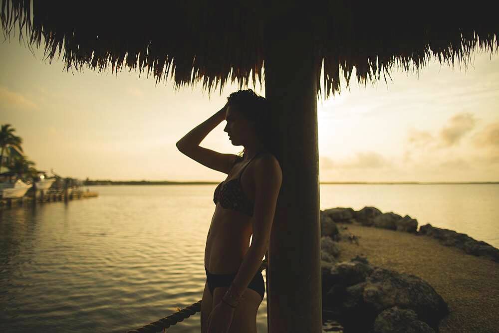 Caucasian woman standing under thatch umbrella on beach