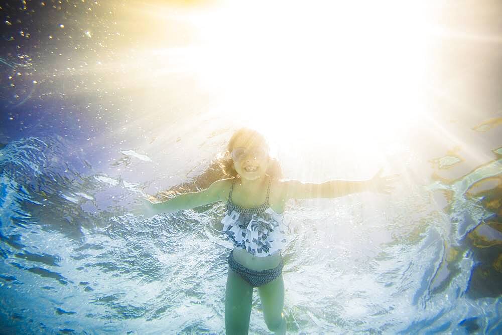 Caucasian girl swimming underwater in swimming pool