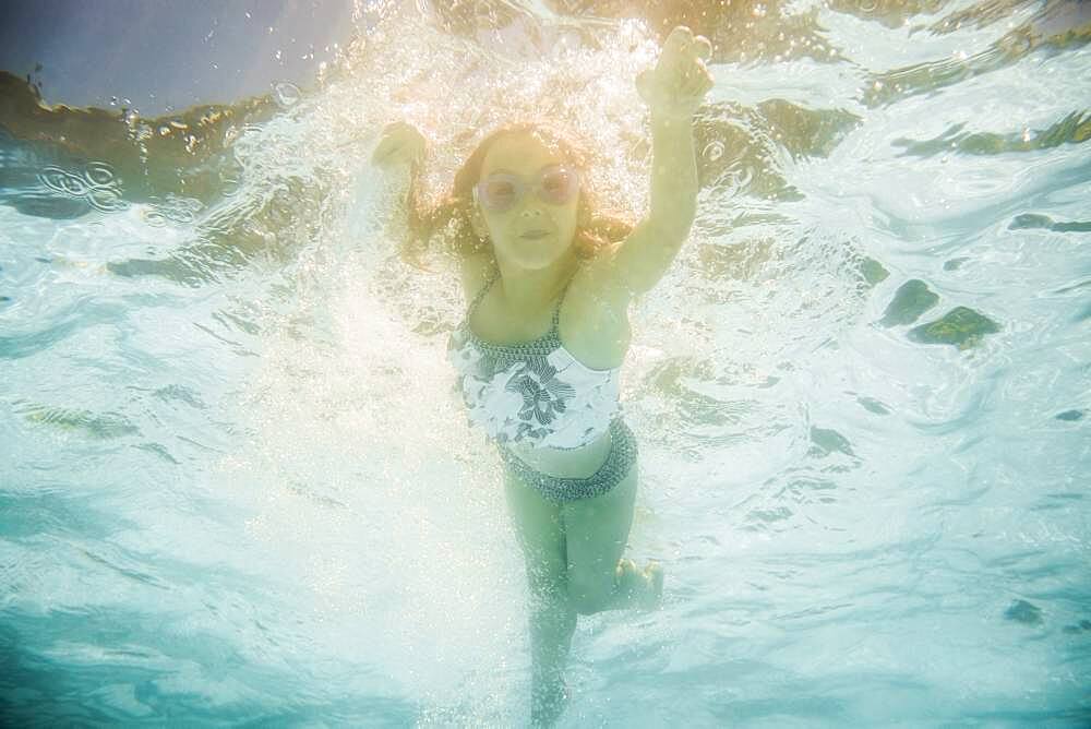 Caucasian girl swimming underwater in swimming pool