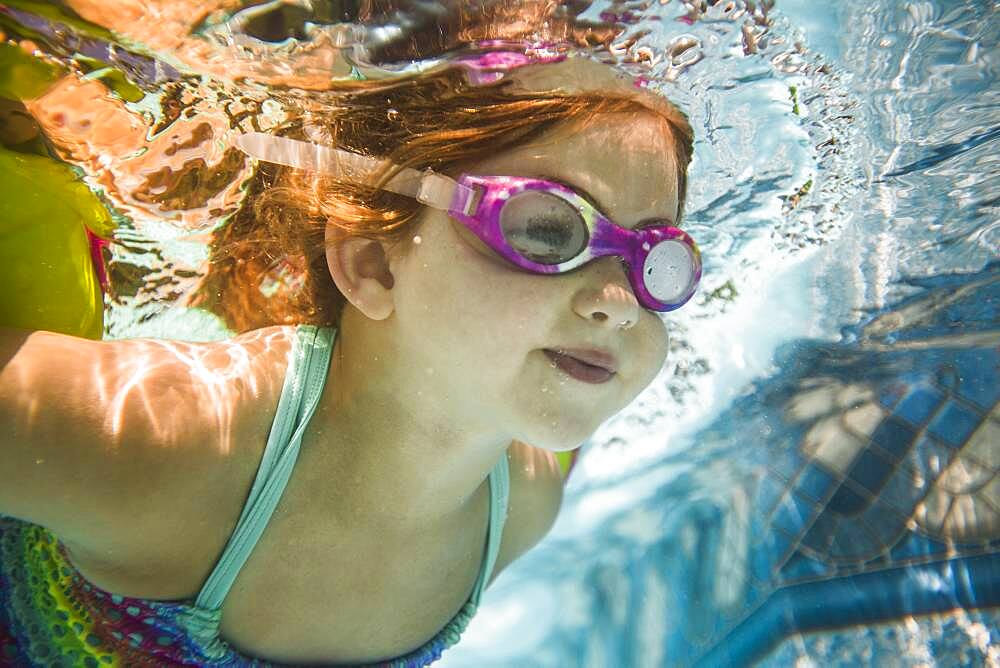 Caucasian girl swimming underwater in swimming pool