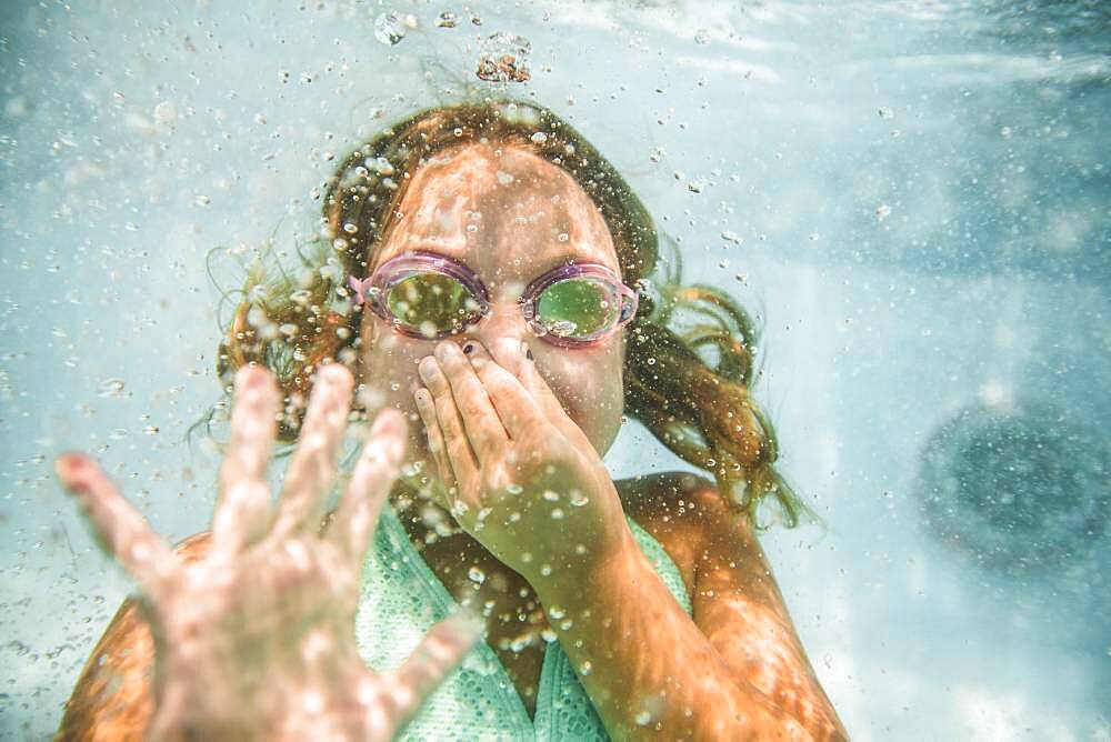 Caucasian girl holding nose underwater in swimming pool