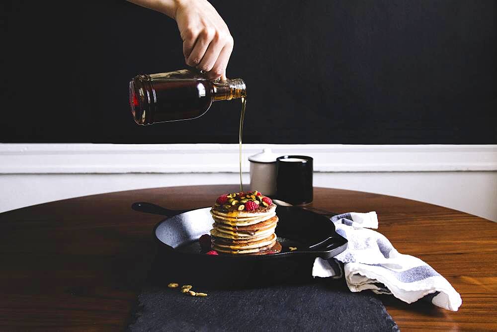 Hand pouring syrup on pancakes