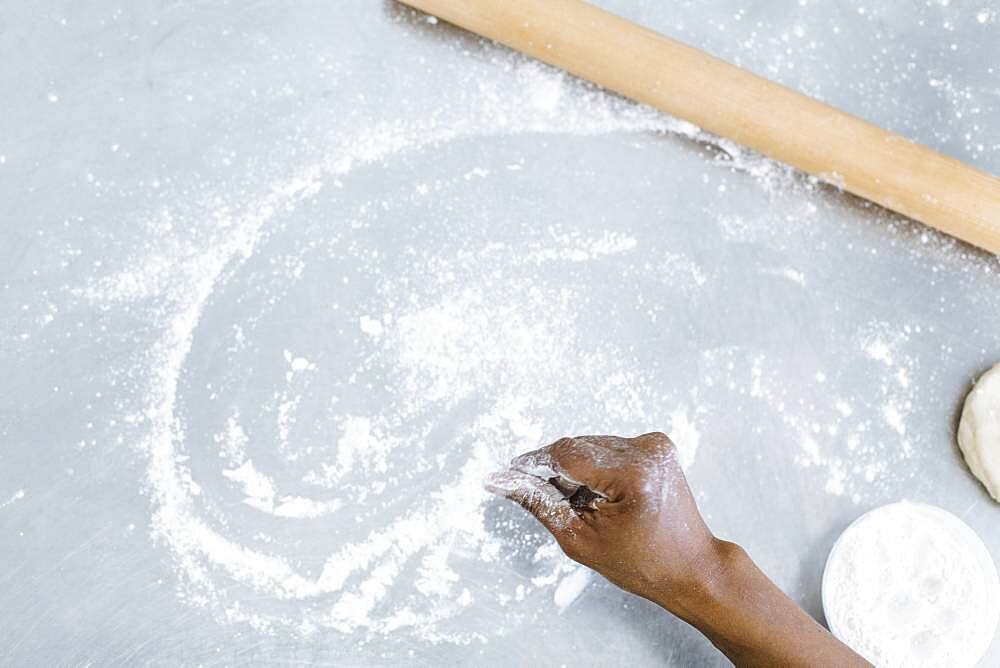 High angle view of baker sprinkling flour on counter