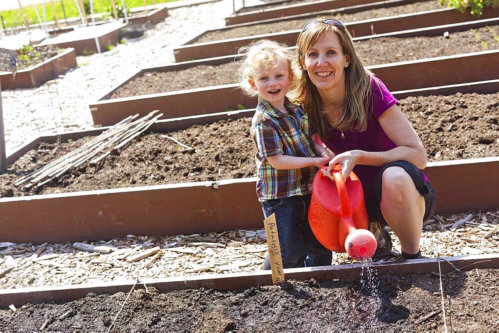 Caucasian mother and son watering plants in garden