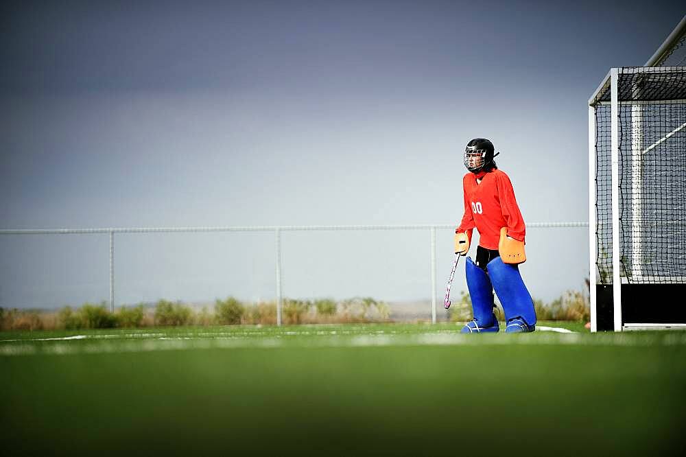 Mixed race field hockey goalie standing by goal