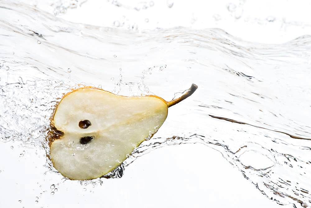 Close up of halved pear splashing in water