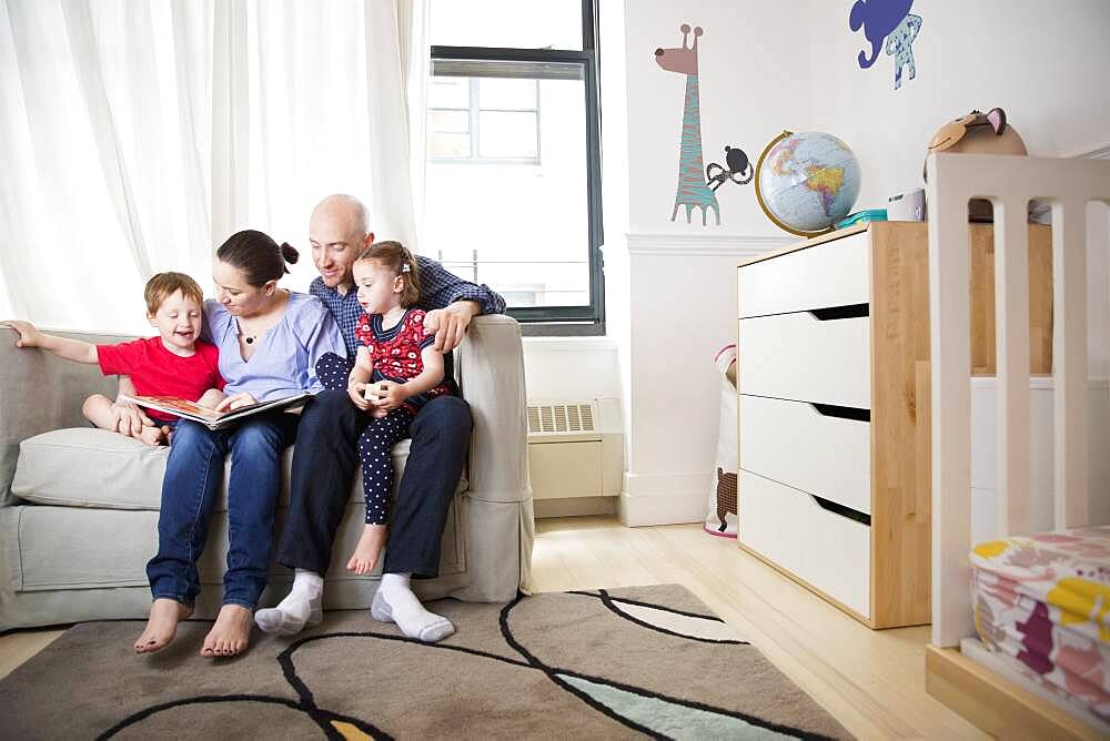 Family reading book on sofa in bedroom