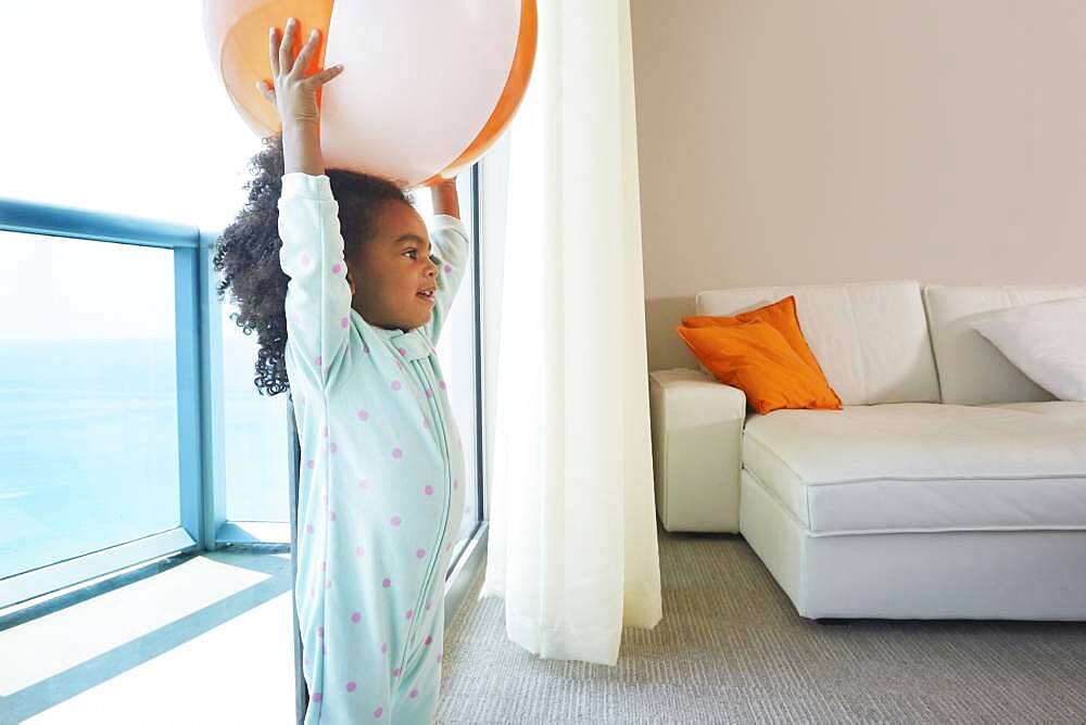 Black girl playing with beach ball in living room