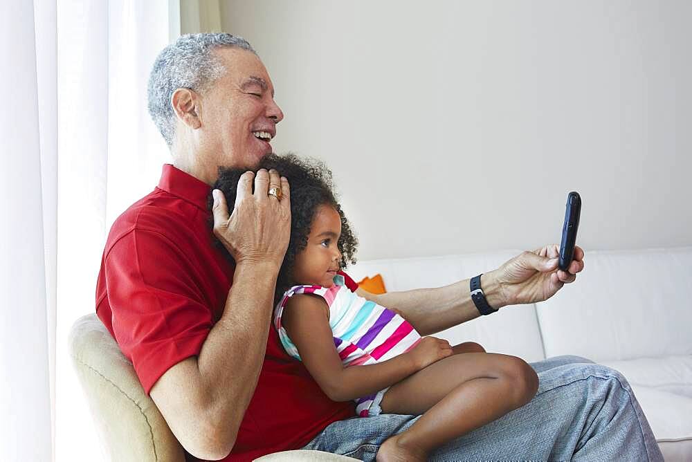 Grandfather and granddaughter taking selfie in living room