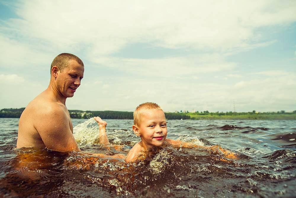 Caucasian father and son swimming in lake