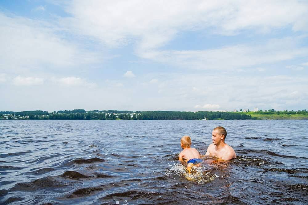 Caucasian father and son swimming in lake