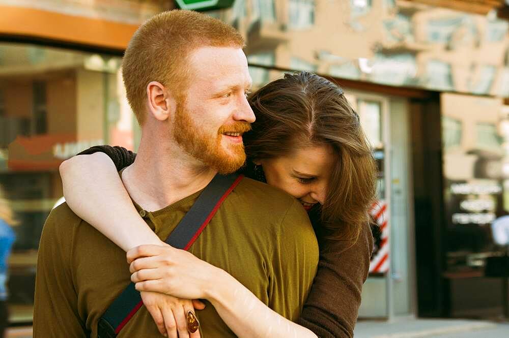 Caucasian couple hugging on city sidewalk