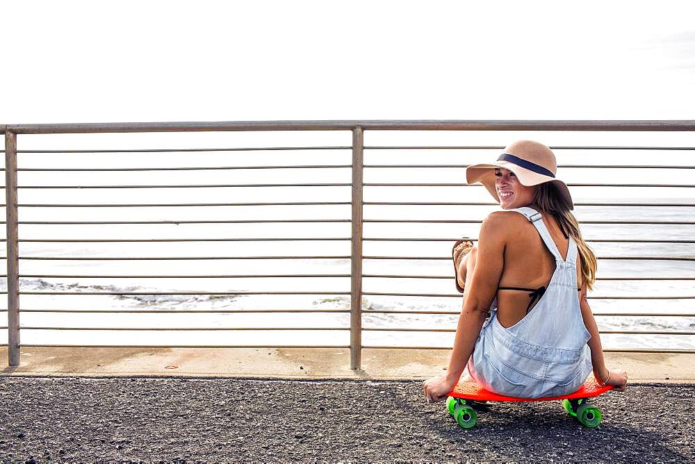 Caucasian woman sitting on skateboard at beach