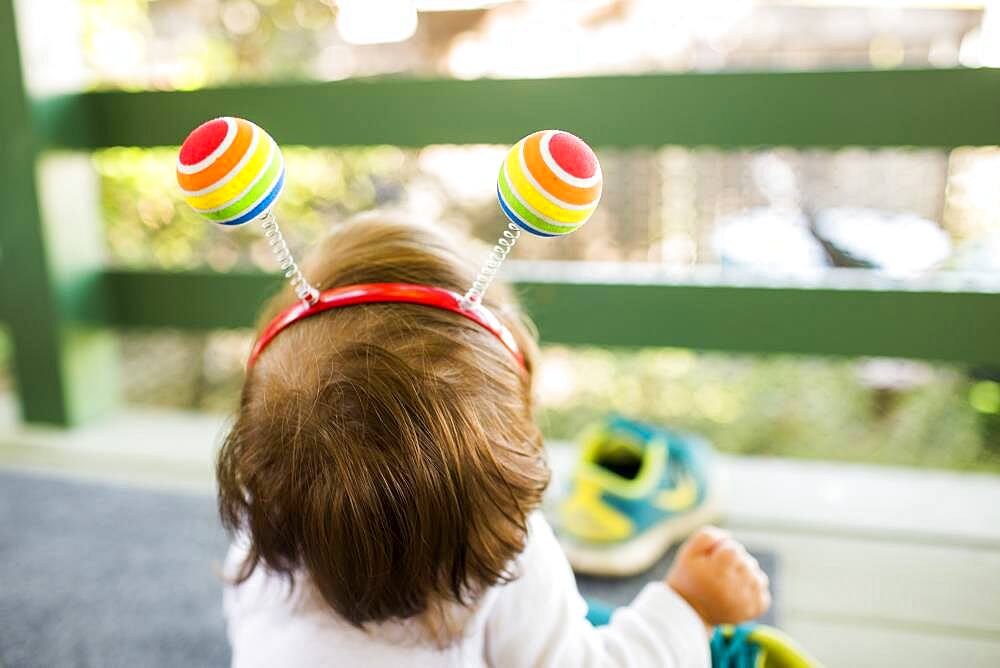 Caucasian baby girl on porch wearing multicolor ball headband