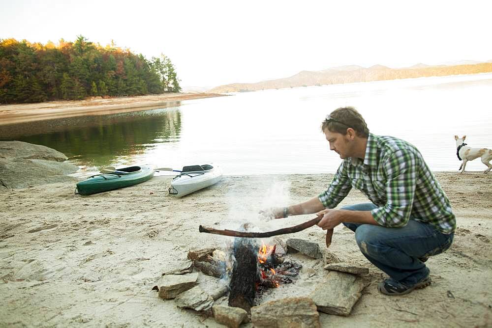 Man building campfire at lake