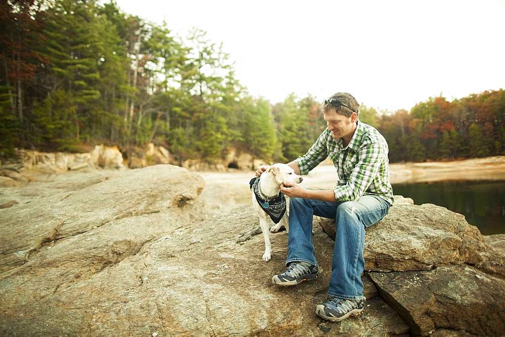 Man petting dog on rocks near lake