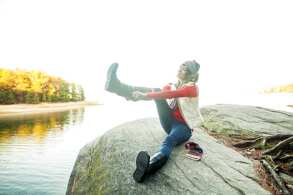 Caucasian woman pulling on boots near lake