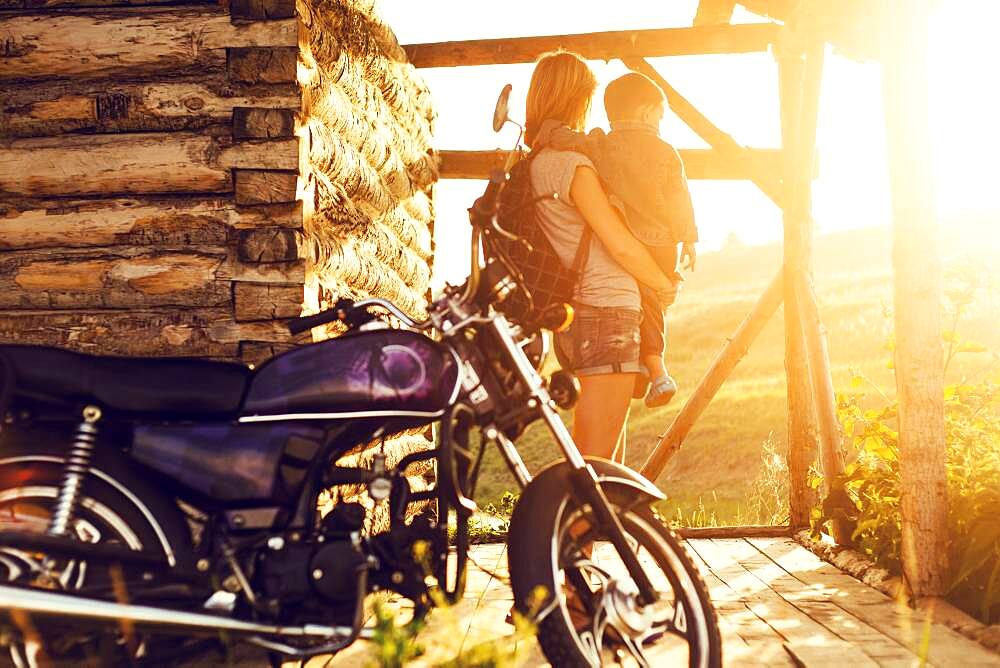 Mother holding son near motorcycle on patio