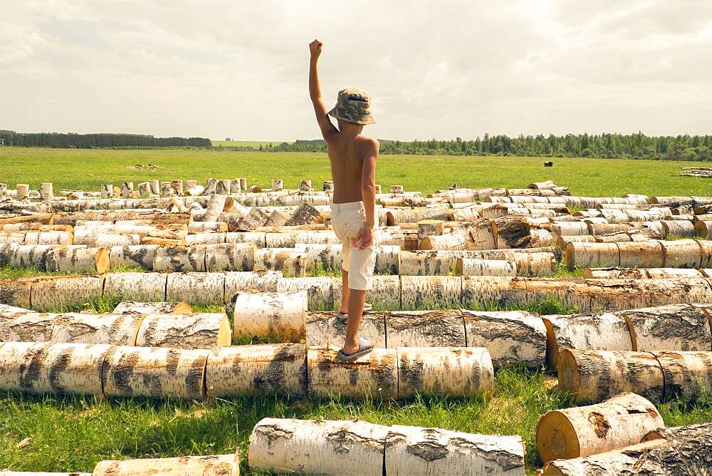 Mari boy standing on logs in rural field