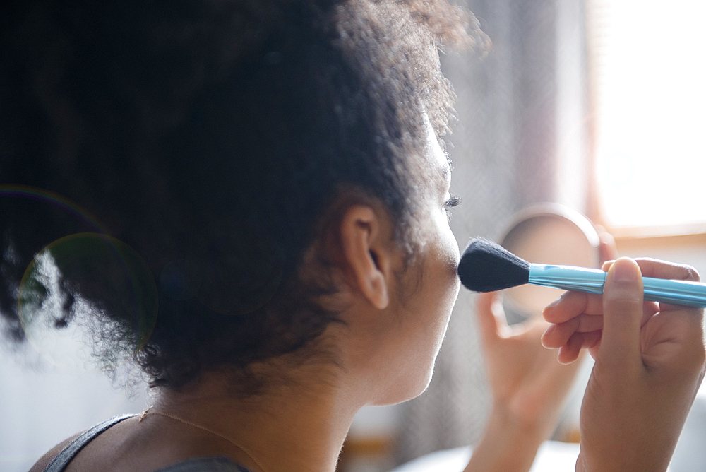 African American woman applying blush to cheek