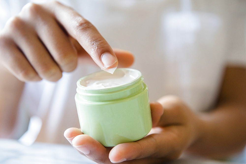 Close up of African American woman dipping finger in lotion jar