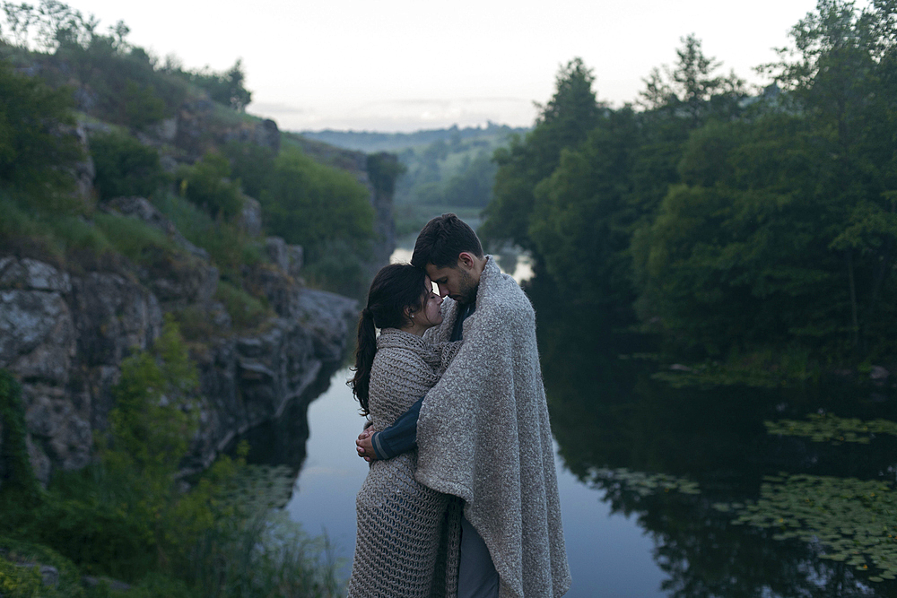 Caucasian couple wrapped in blanket hugging near river