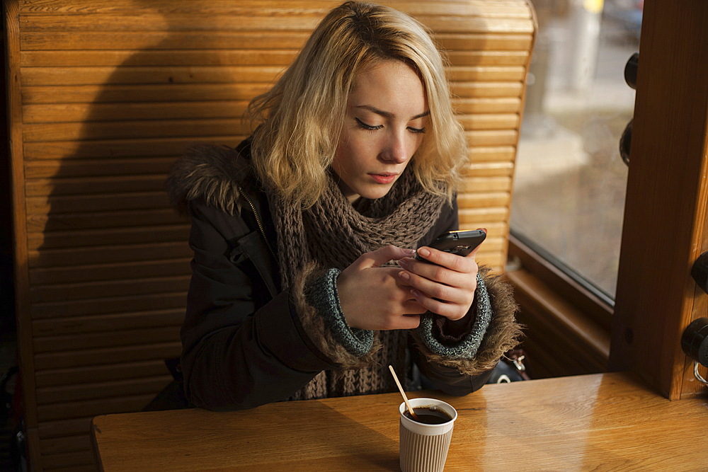 Caucasian woman drinking coffee and texting on cell phone