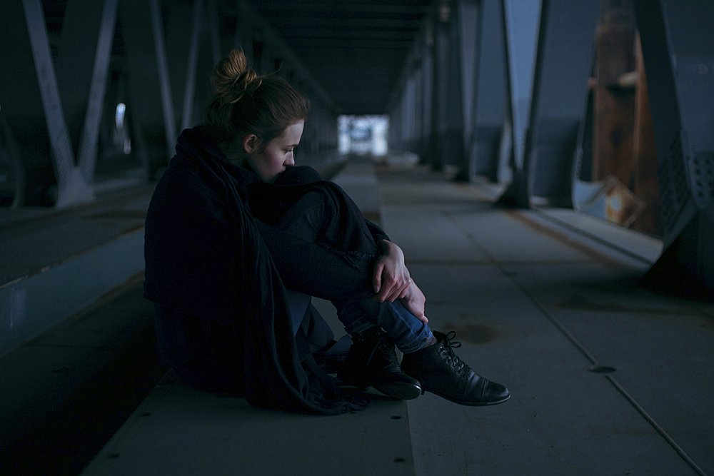 Caucasian woman sitting under bridge