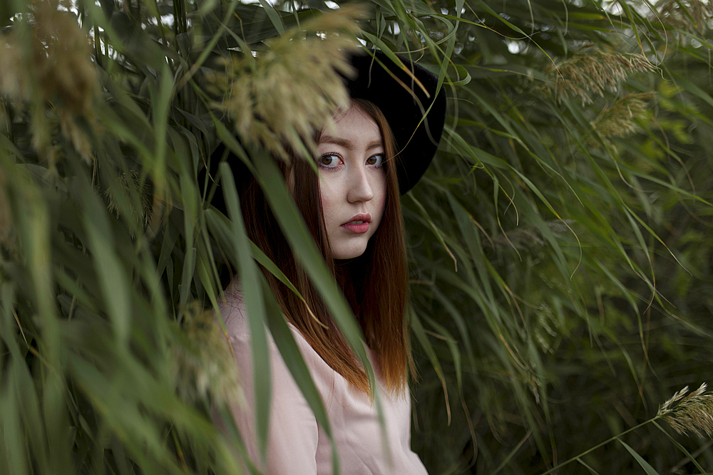 Portrait of serious Asian woman standing in field of tall grass