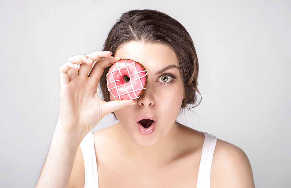 Surprised Caucasian woman holding donut over eye