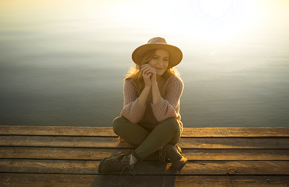 Smiling Caucasian woman sitting on dock of lake