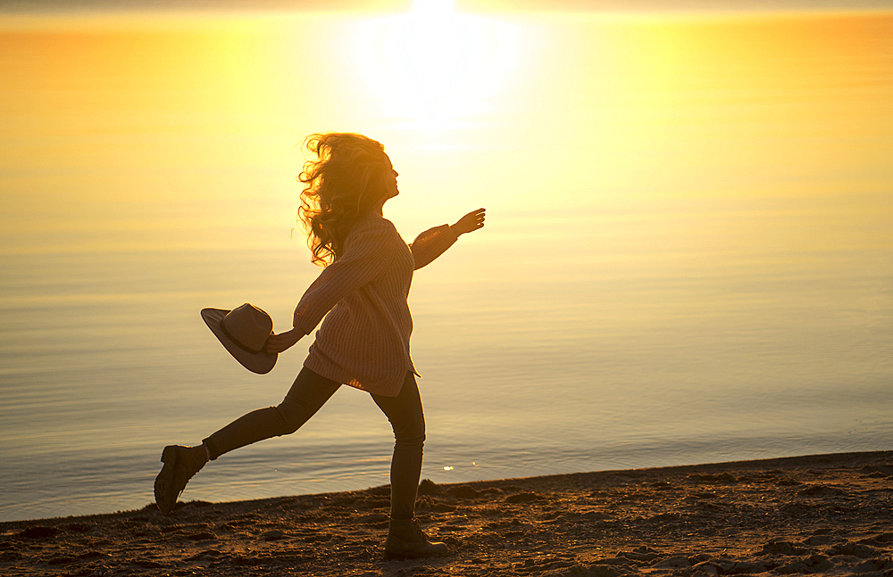 Caucasian woman running on beach holding hat