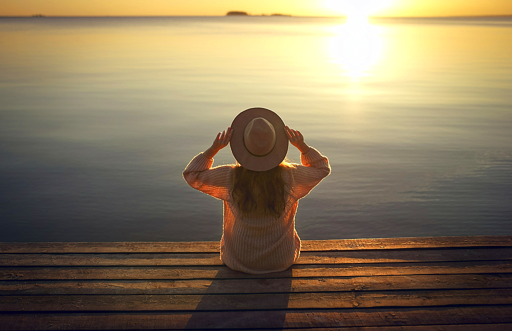 Caucasian woman sitting on dock of lake admiring sunset