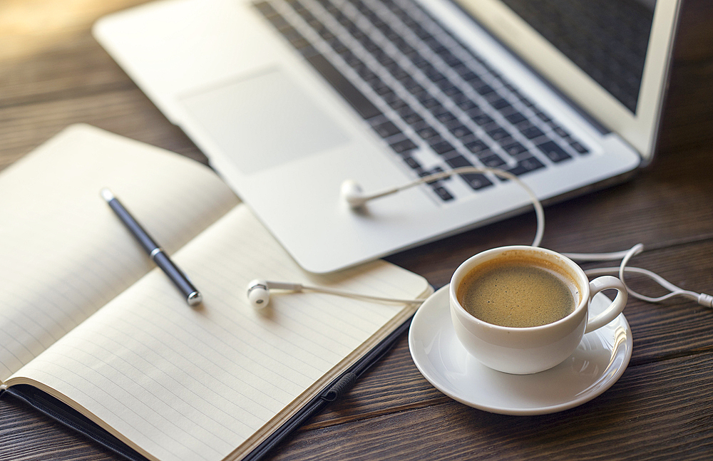 Earbuds with notebook and coffee near laptop