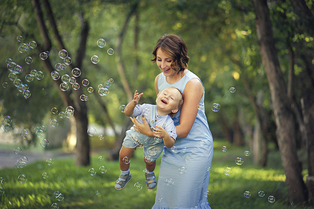 Caucasian mother holding baby son playing with bubbles