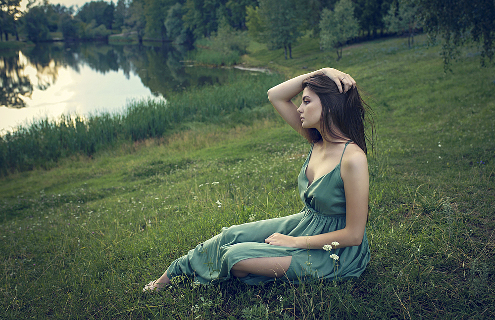 Caucasian woman sitting in grass with wildflowers near lake