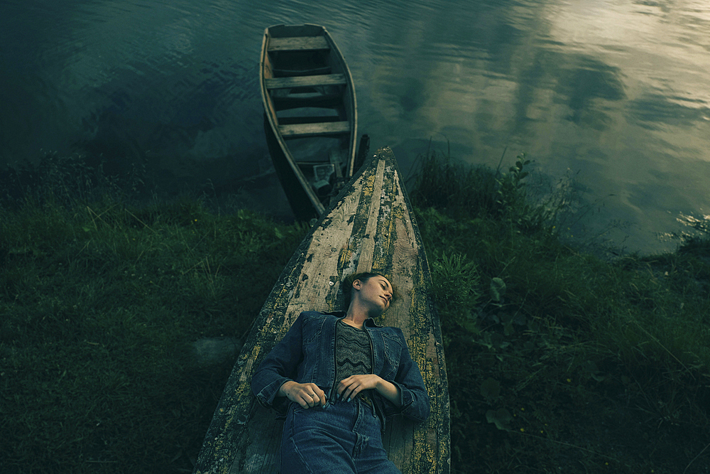 Caucasian woman laying on upside-down boat near lake