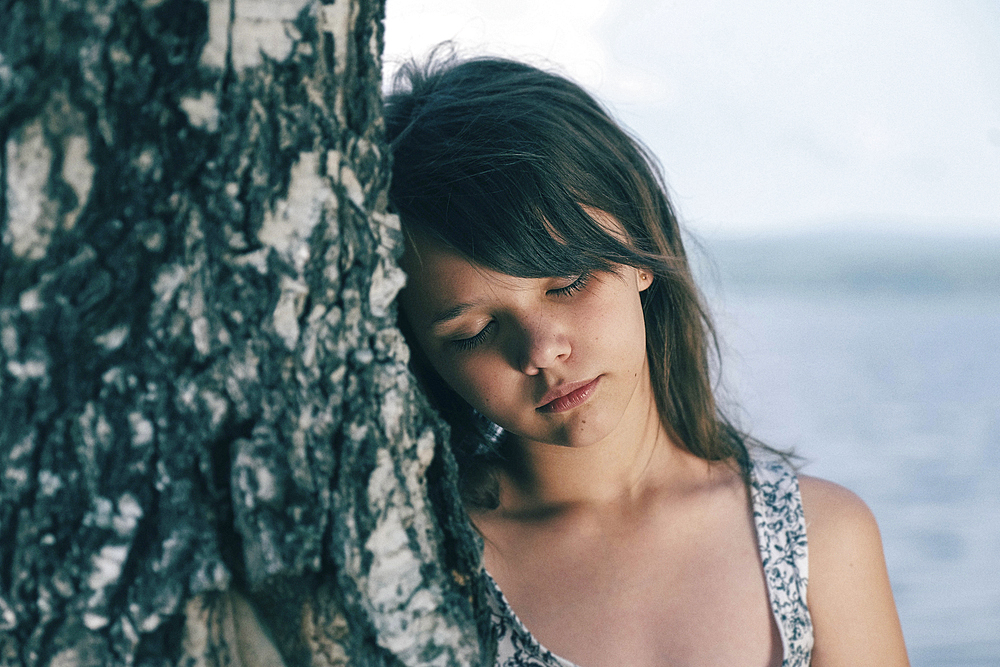 Caucasian girl leaning head on tree trunk