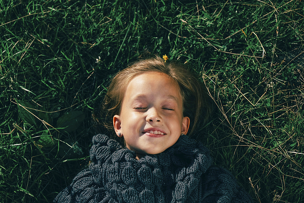 Caucasian girl wearing sweater laying in grass