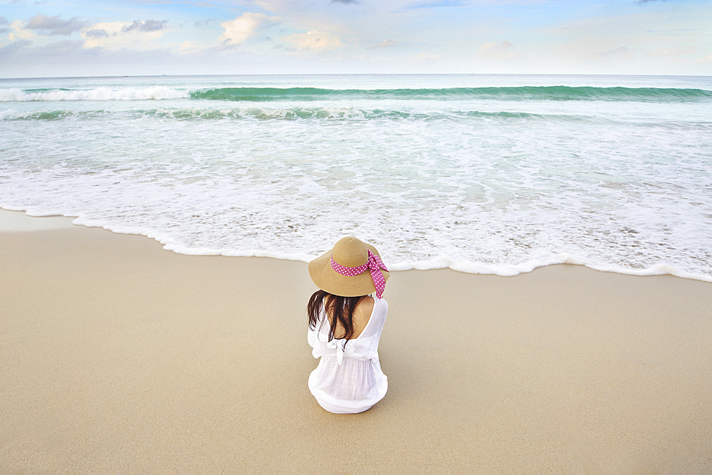 Woman sitting on beach near ocean waves